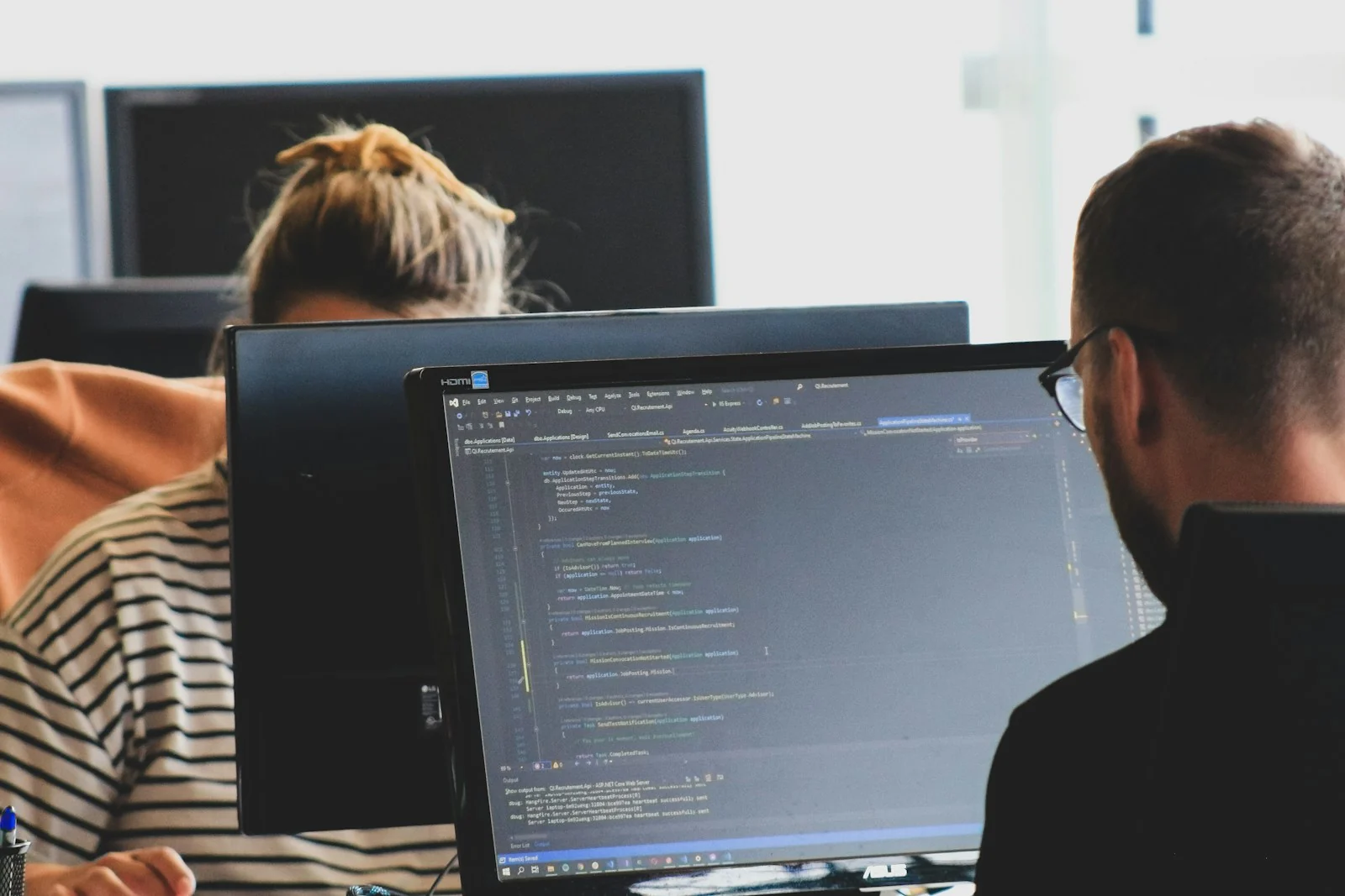 Two colleagues working at computer screens with source code visible